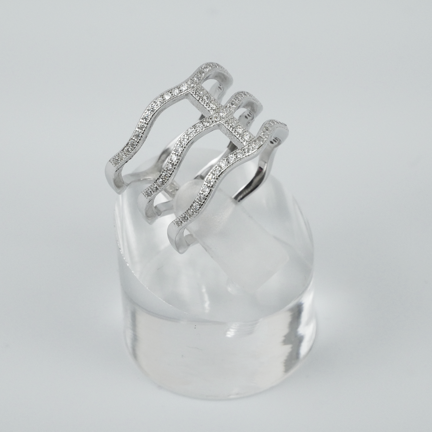 Silver ring with intricate design on a clear stand against a light-grey background