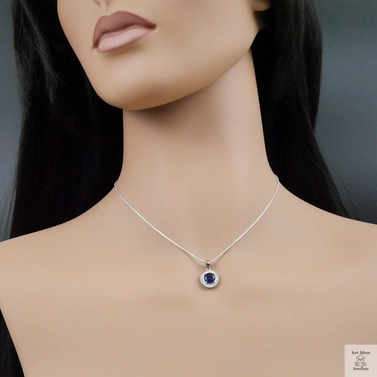 Mannequin wearing a silver necklace with a blue pendant on a dark background