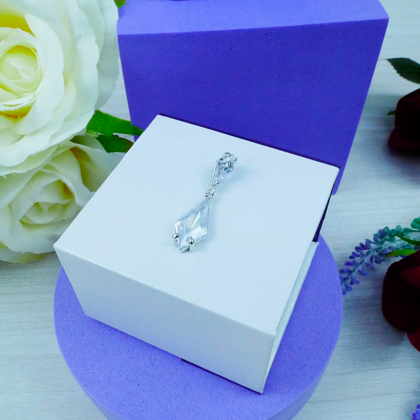 Silver earrings on a white box with purple base and white roses in the background