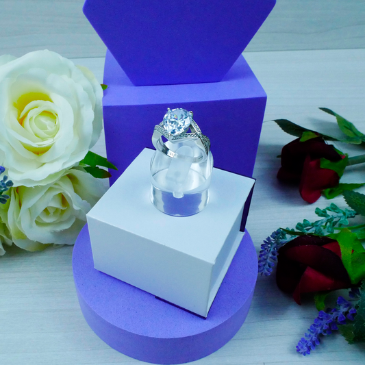 Diamond ring on a white stand with purple base, surrounded by flowers