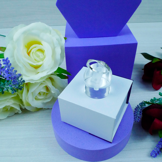 Silver ring on a white box with purple base, surrounded by flowers