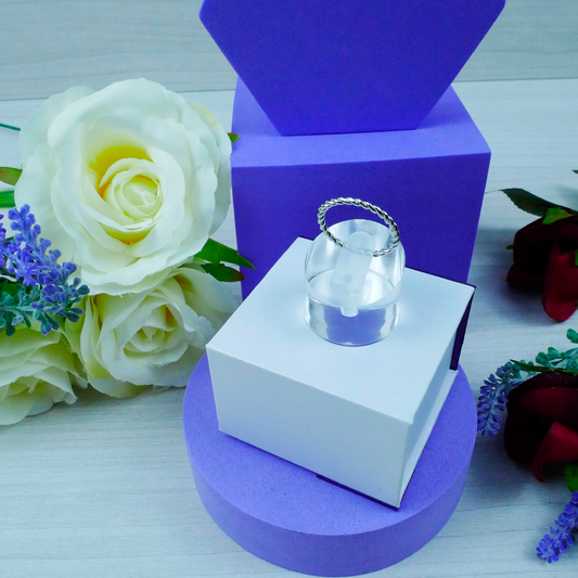 Clear ring on a white box with a purple stand, surrounded by flowers