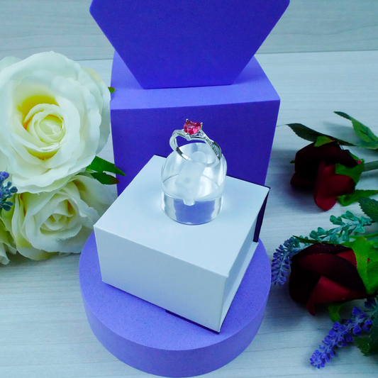 Ring on a clear stand with purple and white boxes and flowers in the background