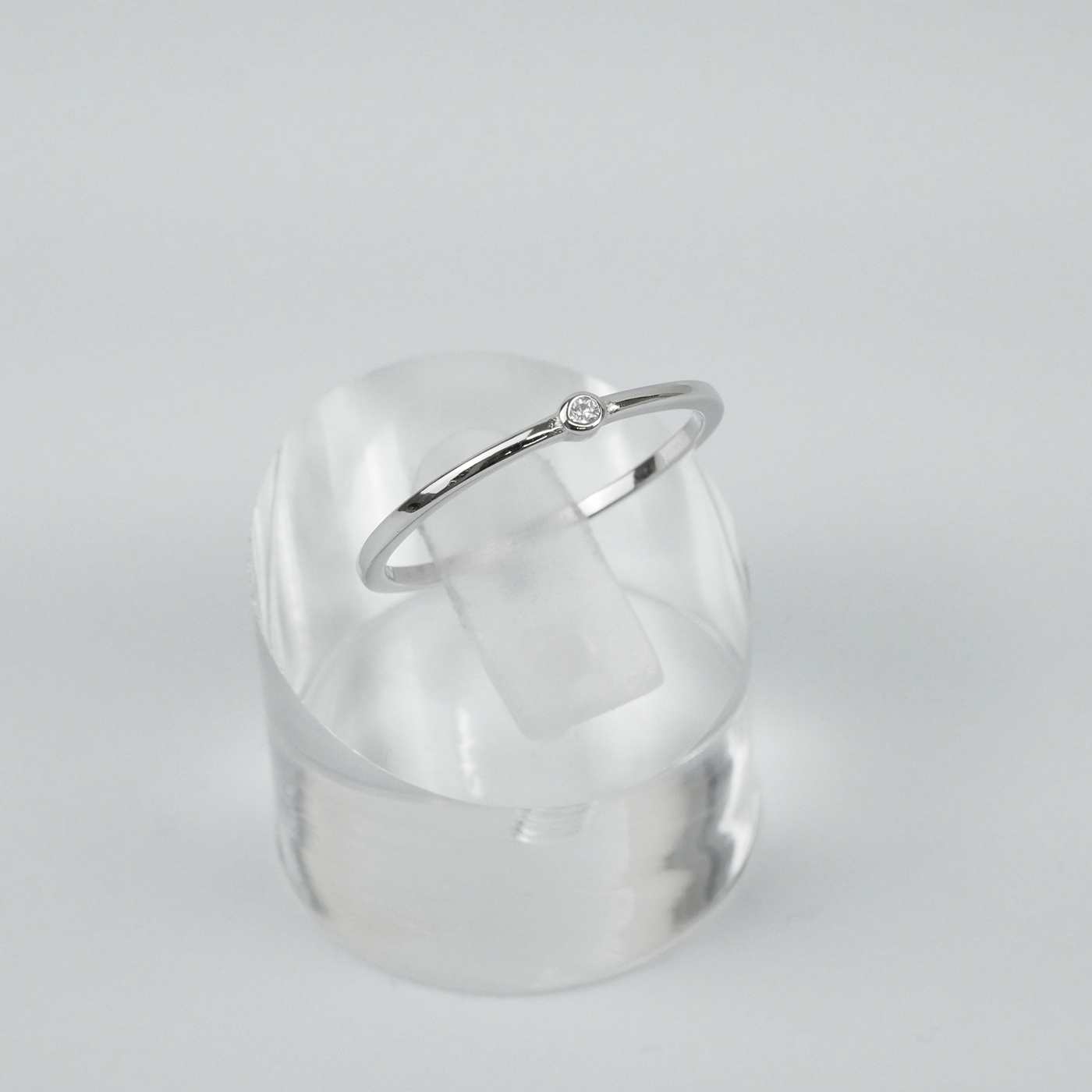 Silver ring on a clear acrylic stand against a light grey background