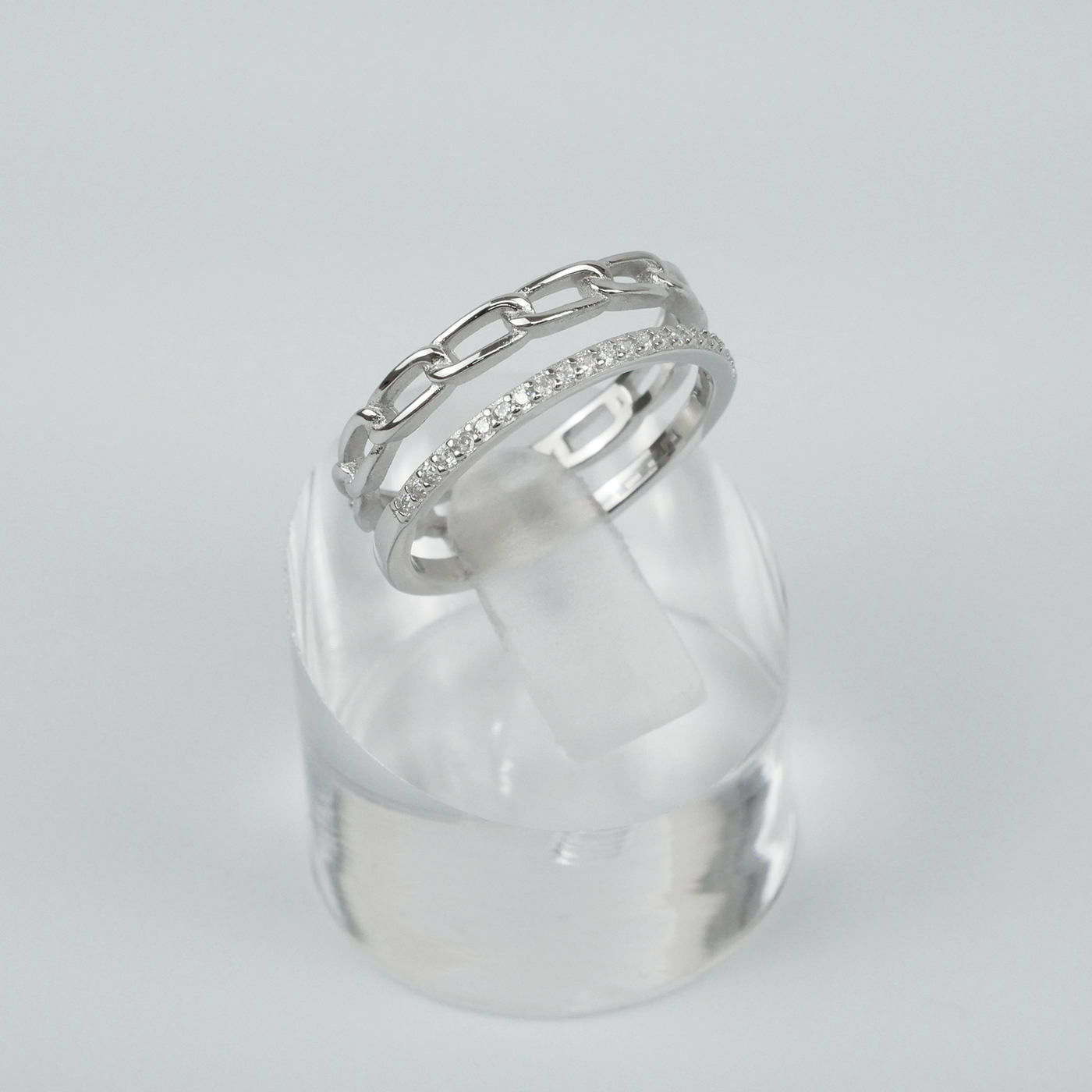 Silver ring with gemstones on a clear stand against a light grey background