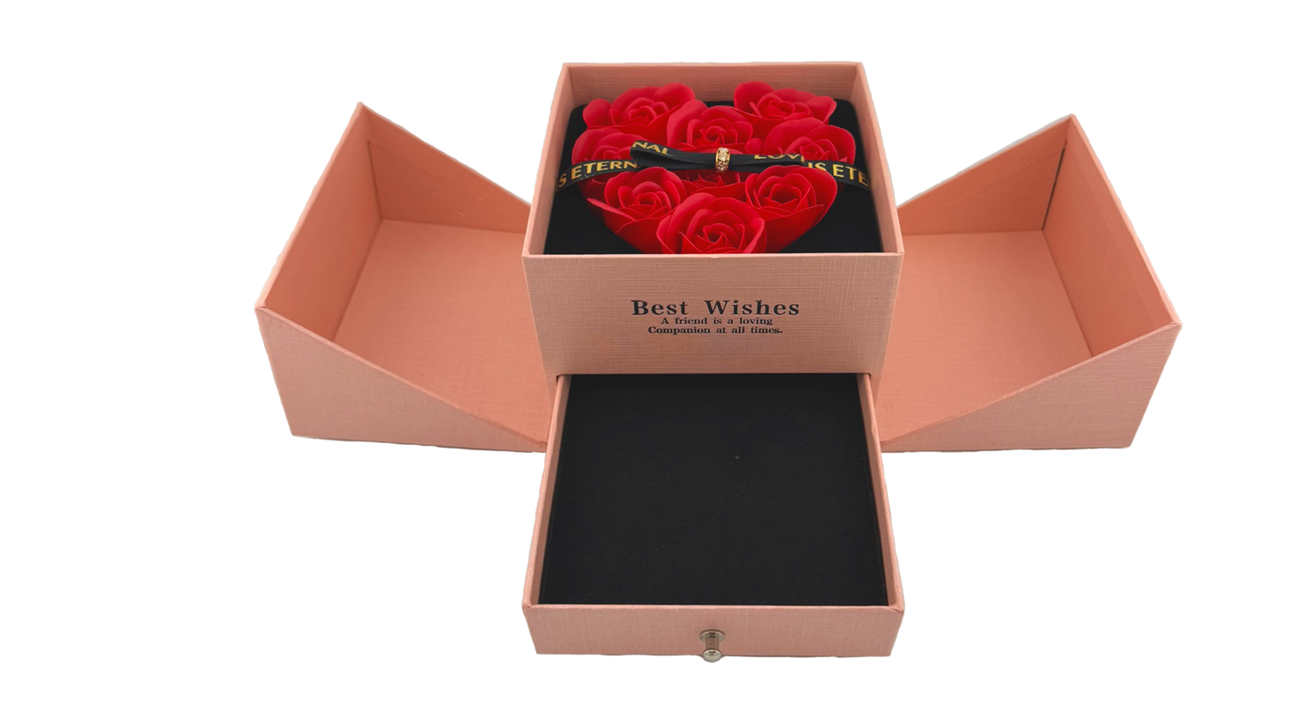 A red jewellery box with a heart-shaped arrangement of red roses on the lid, secured with a magnetic bow. The box is open, revealing cutouts for holding jewelry items like chains, earrings, and rings.
