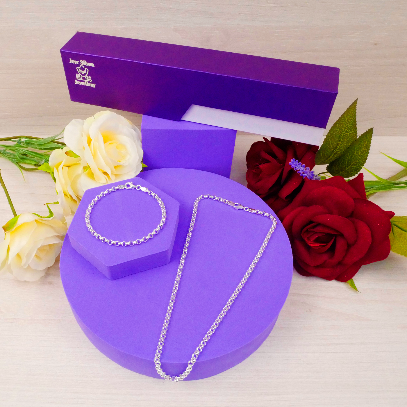 Silver necklace on a purple stand with a purple box and flowers in the background