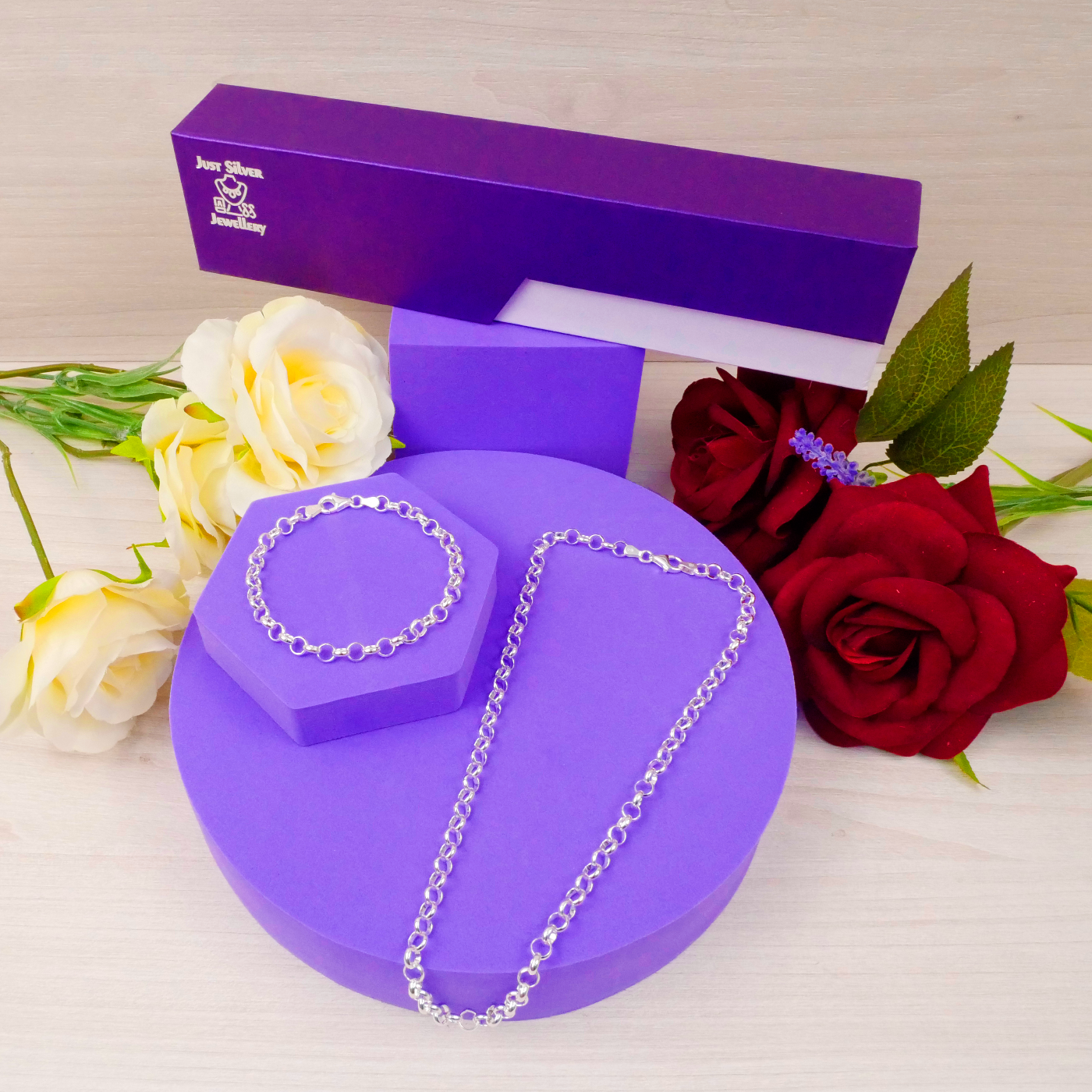 Silver necklace on a purple stand with a purple box and flowers in the background