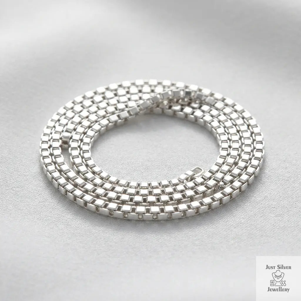 Sterling silver box chain necklace coiled on a light grey background