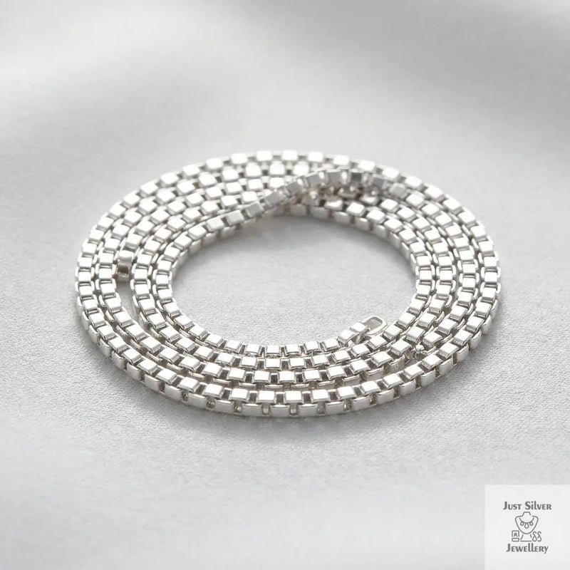 Sterling silver box chain necklace coiled on a light grey background