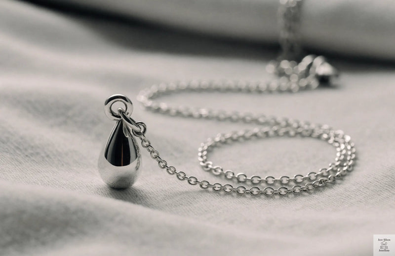 Sterling silver pendant necklace with a delicate chain laid on a soft grey surface