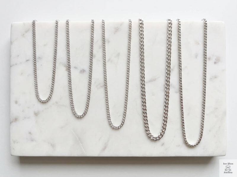 Sterling silver chain necklaces of different lengths laid out to compare choker, princess and matinee lengths