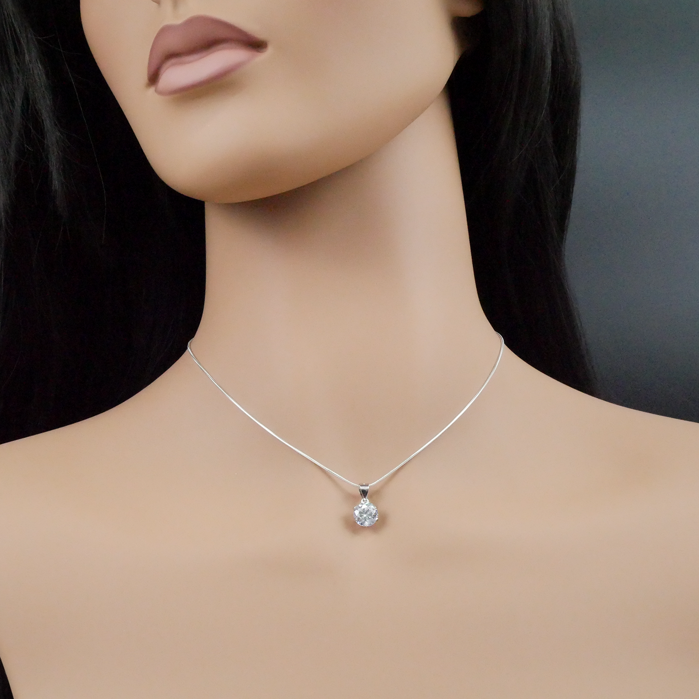 Mannequin wearing a silver necklace with a zirconia pendant on a dark background