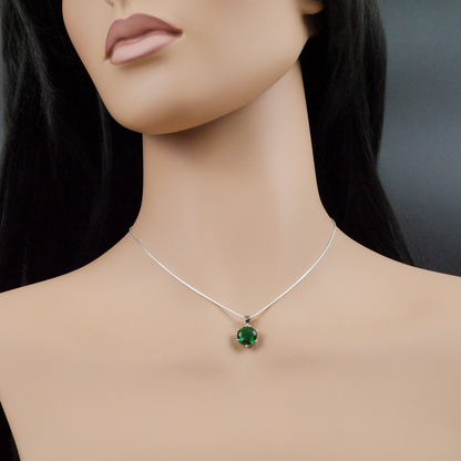 Mannequin wearing a silver necklace with a green pendant against a dark background