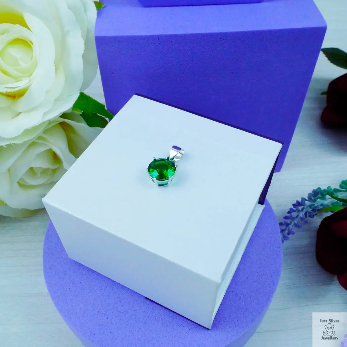 Green gemstone pendant in a white box with purple and floral background