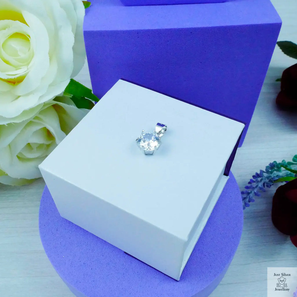 Silver earring in a white box with purple base and white roses in the background