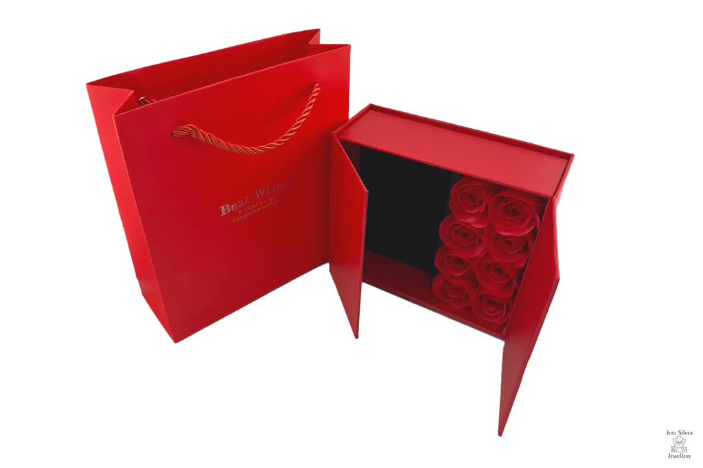 A red jewellery box with eight rose petals inside, accompanied by a matching red presentation bag with a rope handle.