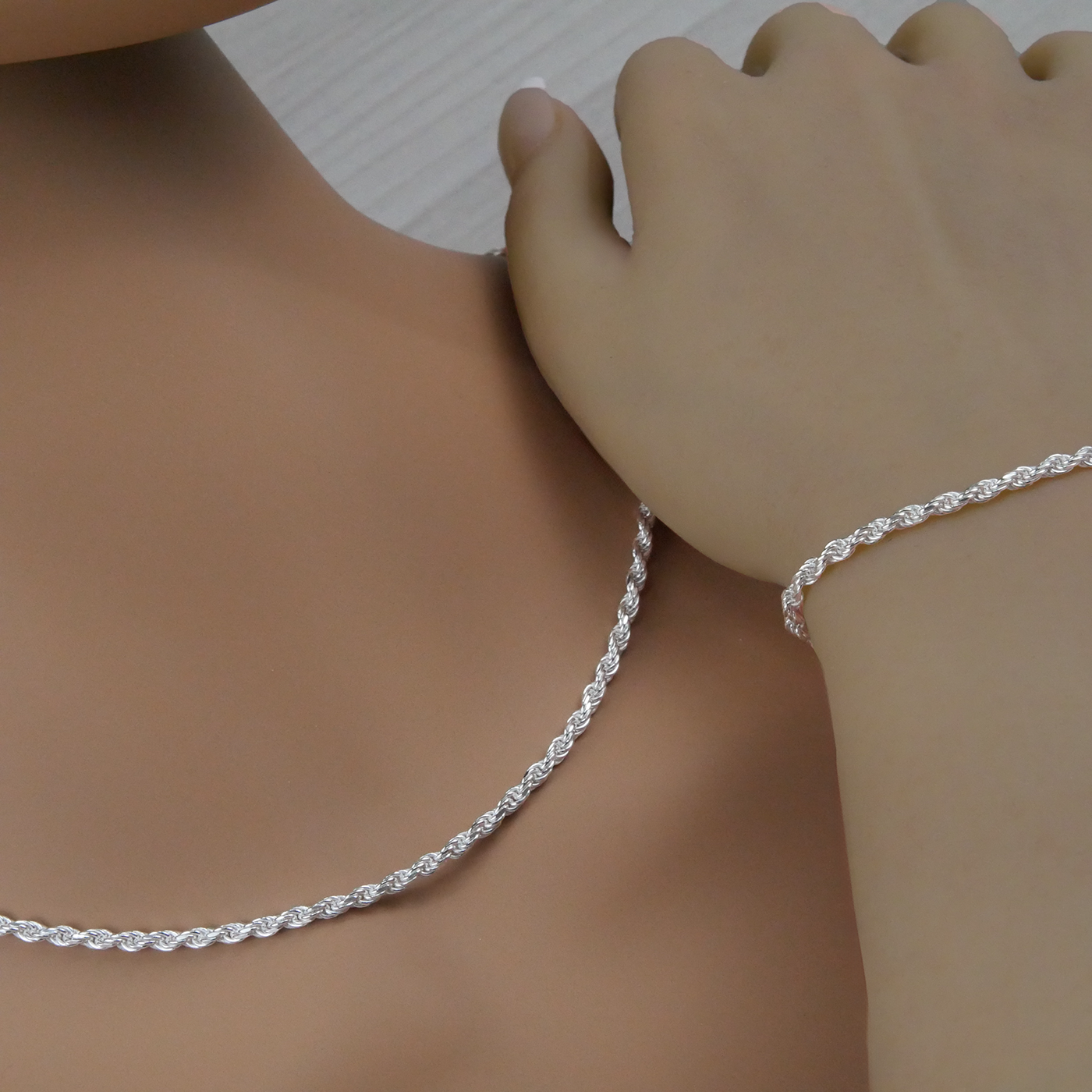 Silver rope necklace and bracelet on a person's neck and wrist against a neutral background