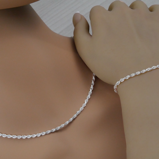 Silver rope necklace and bracelet on a person's neck and wrist against a neutral background