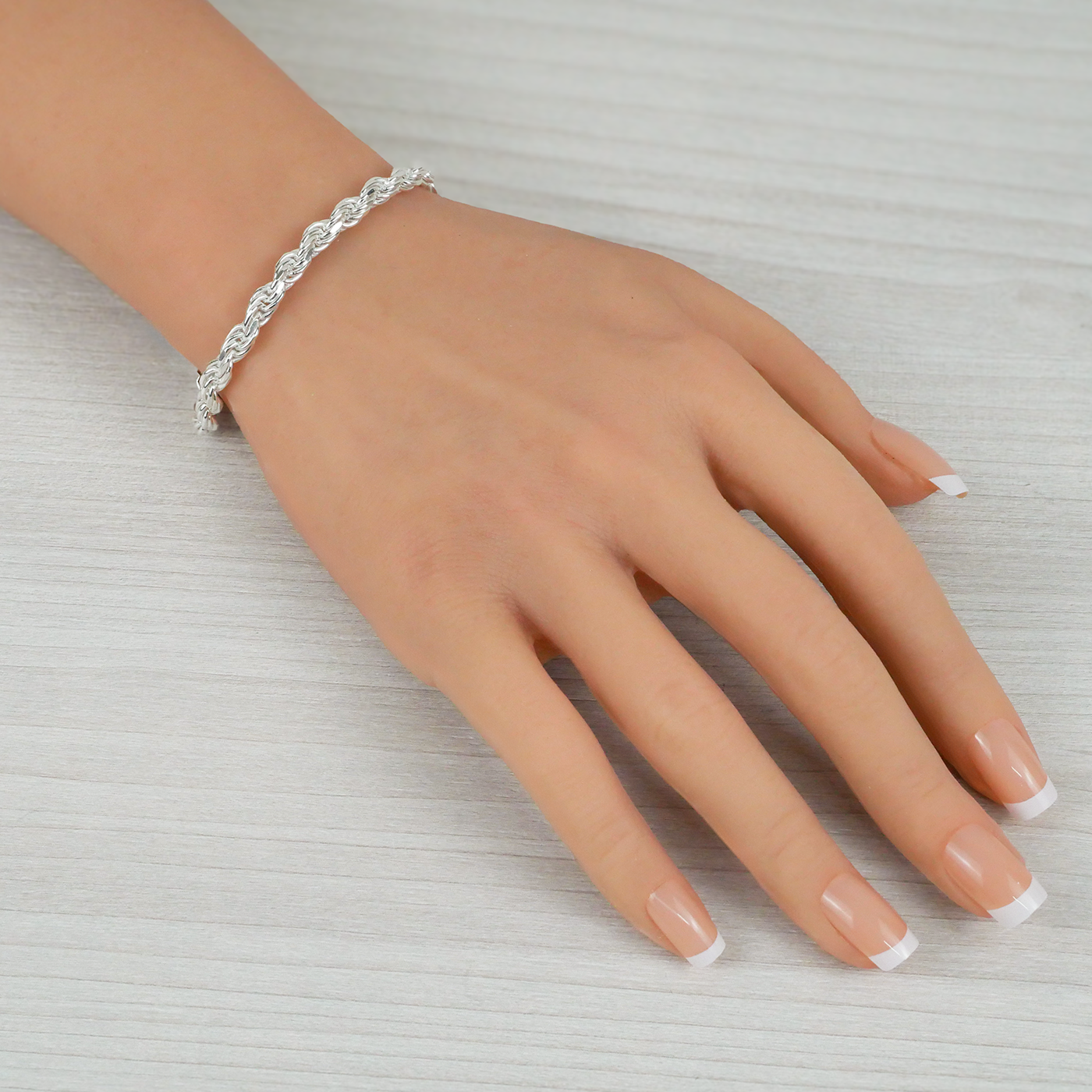 Hand wearing a silver bracelet on a light gray background