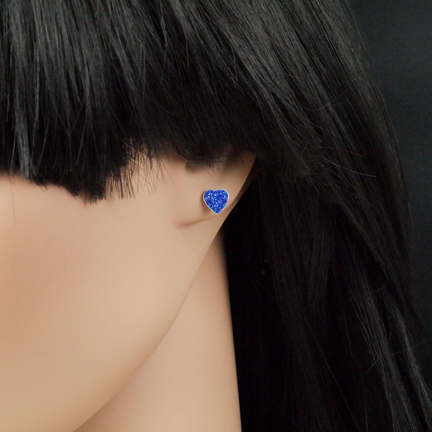 Blue heart-shaped earring worn by a person with black hair on a dark background