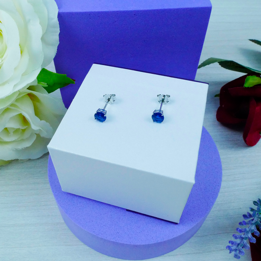 Pair of blue gemstone earrings in a white box with purple base and floral decorations.