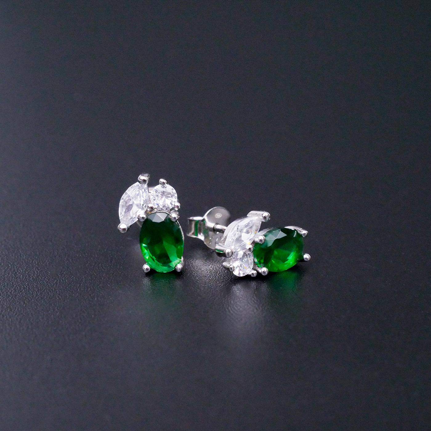 Pair of green gemstone earrings with silver settings on a dark background