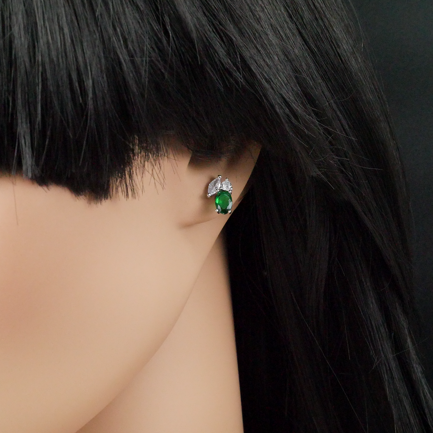 Close-up of a person wearing a green gemstone earring with a dark background