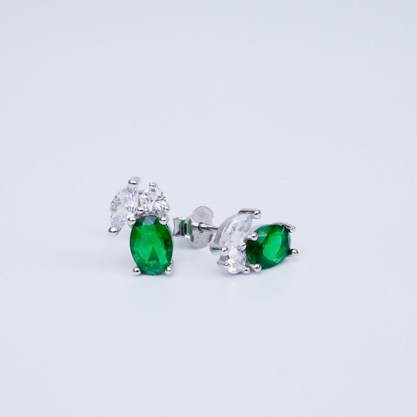 Pair of emerald and zirconia stud earrings on a light grey background