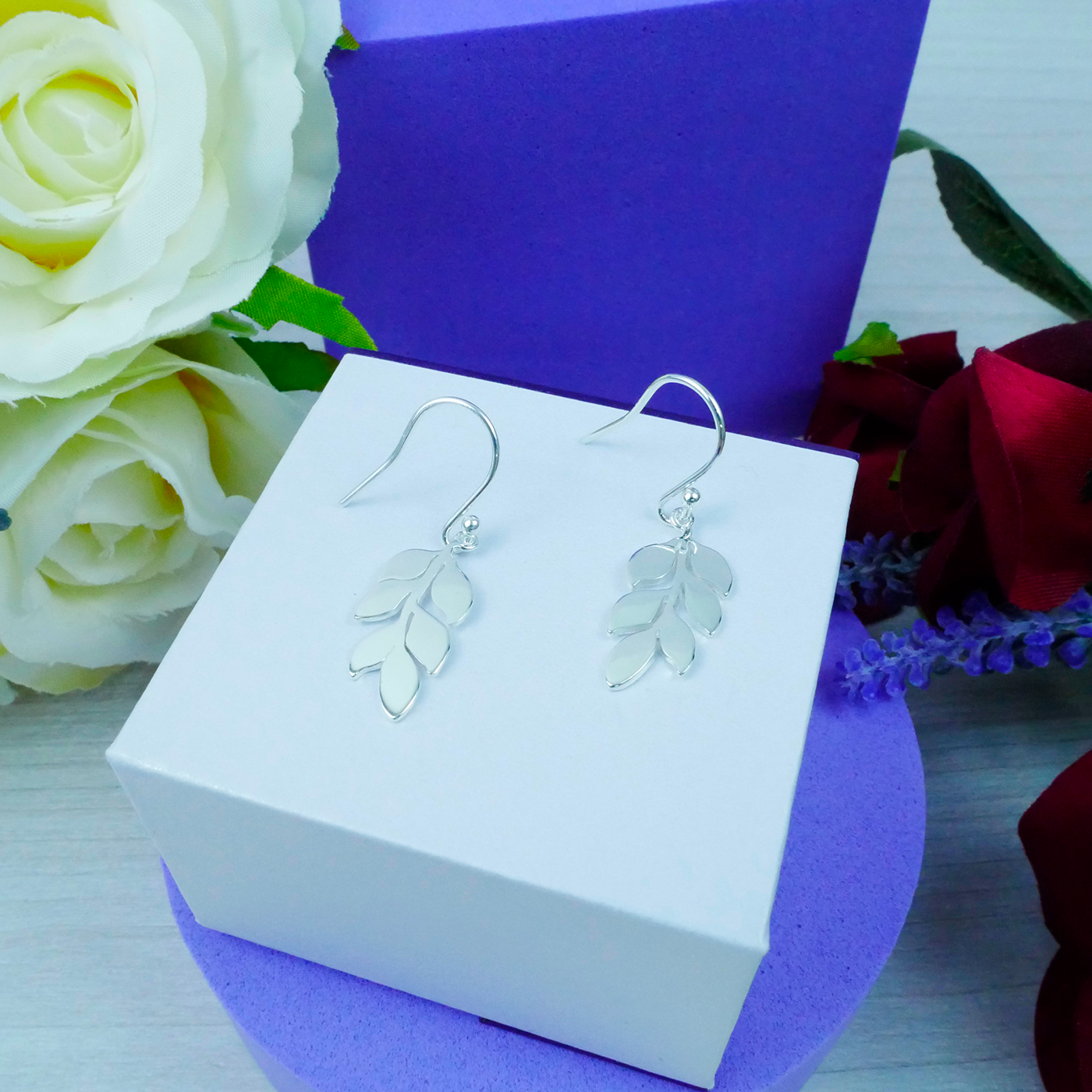 Silver leaf earrings on a white box with flowers in the background