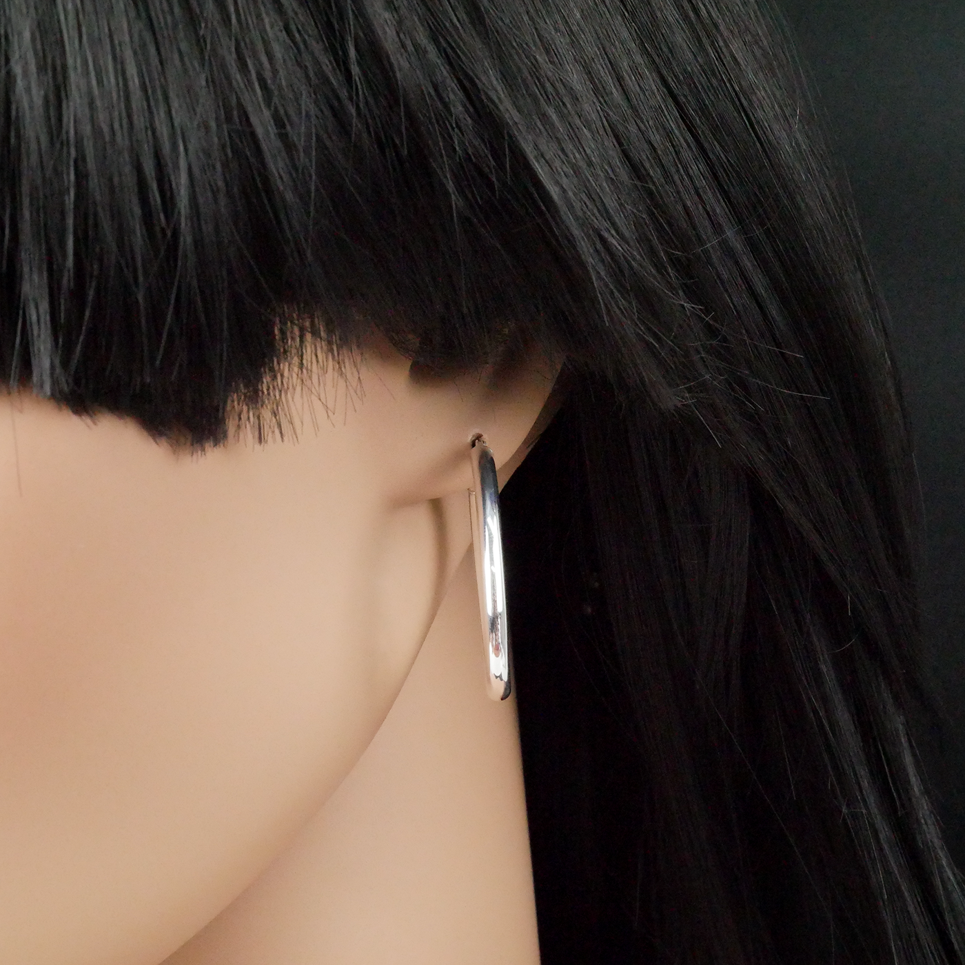 Silver hoop earring worn by a person with black hair on a dark background