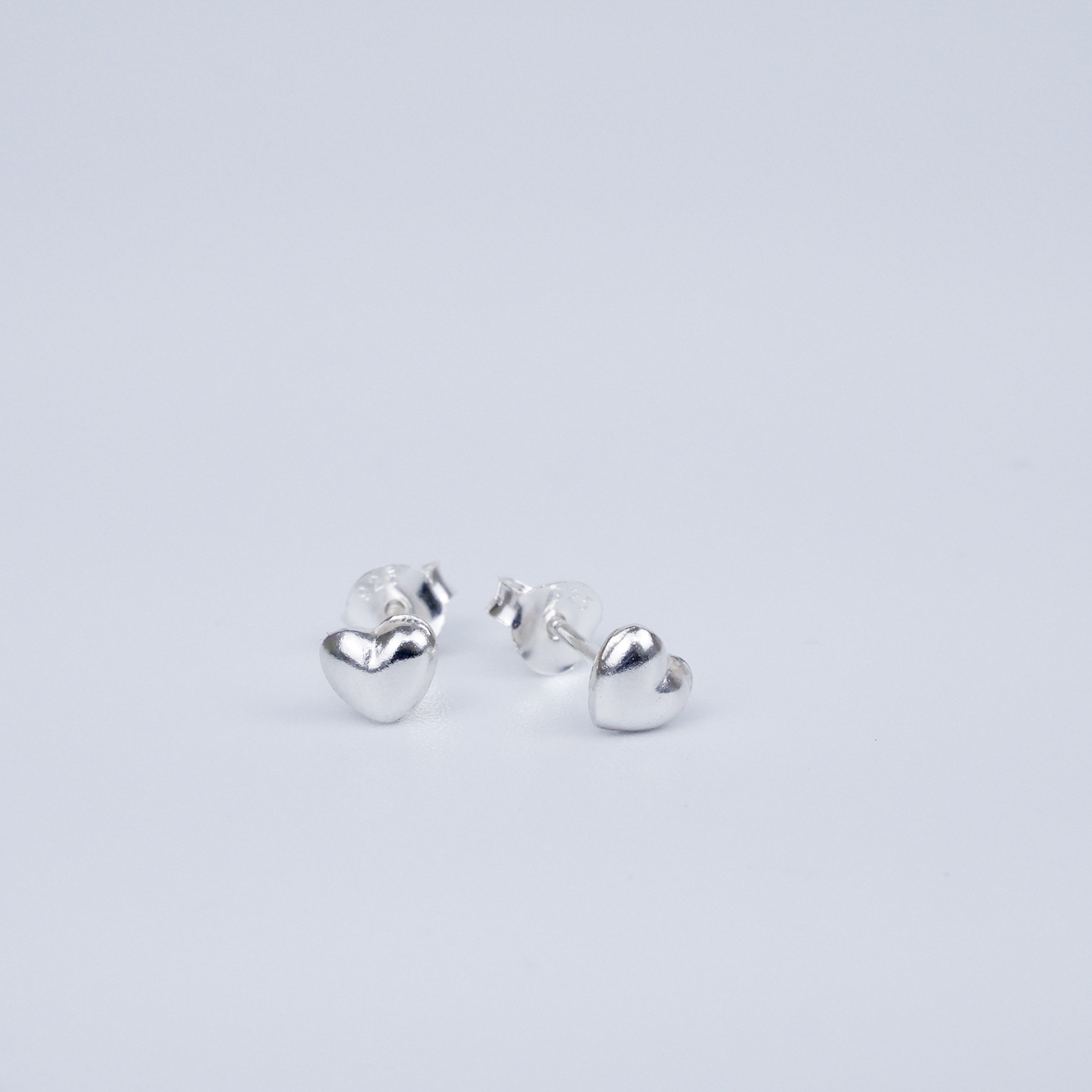 Heart-shaped silver earrings on a light grey background