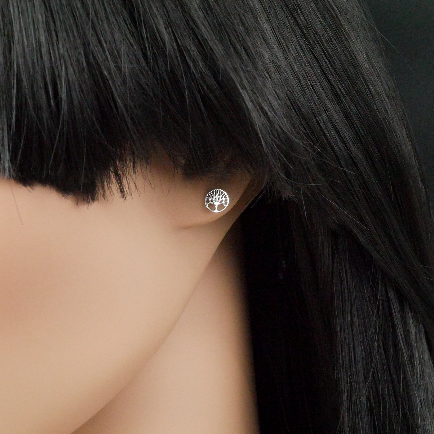 Silver tree-of-life earring on a mannequin ear against a dark background