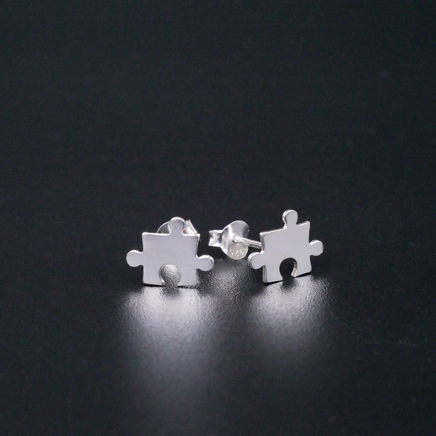 Silver puzzle piece earrings on a black background