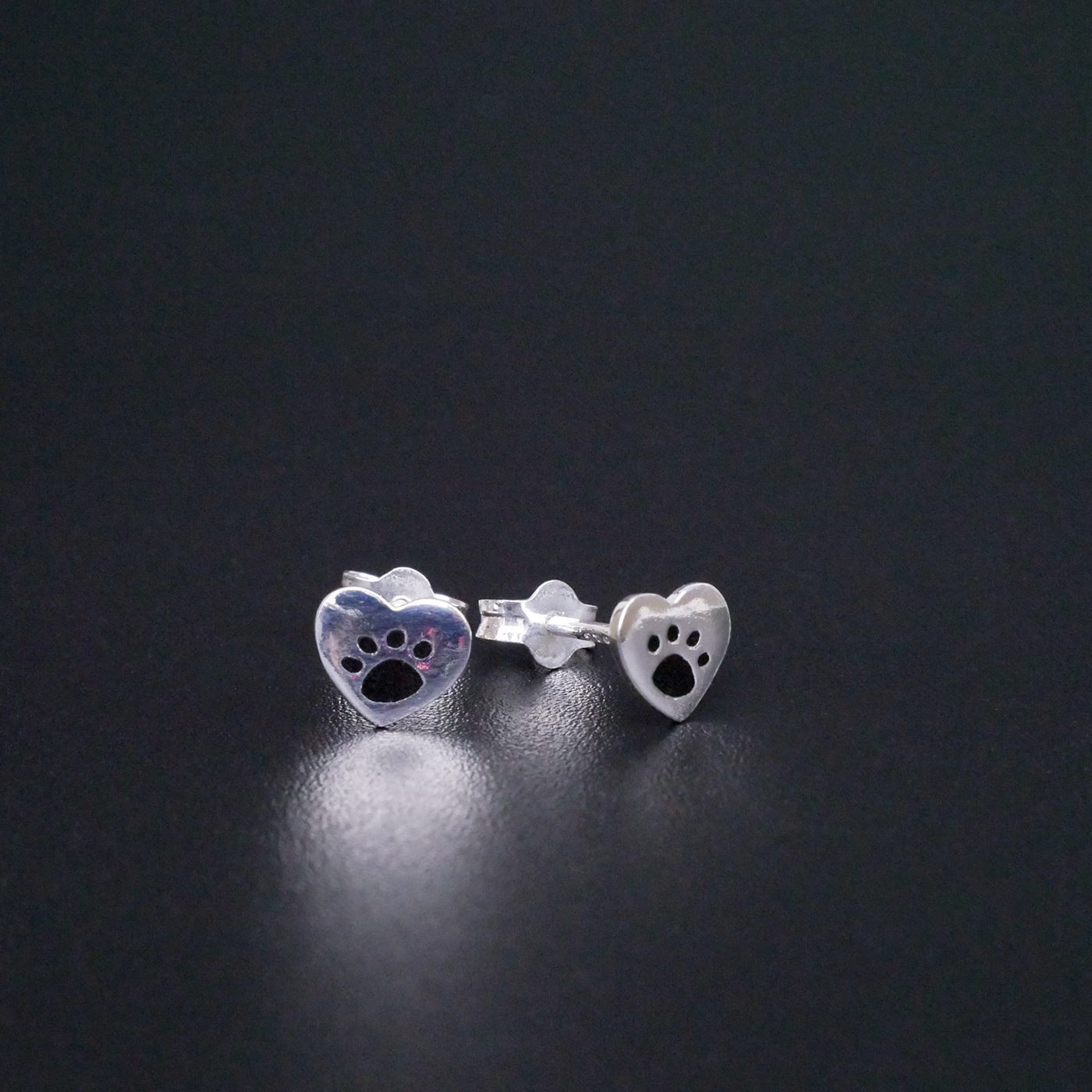 Silver paw print earrings on a black background