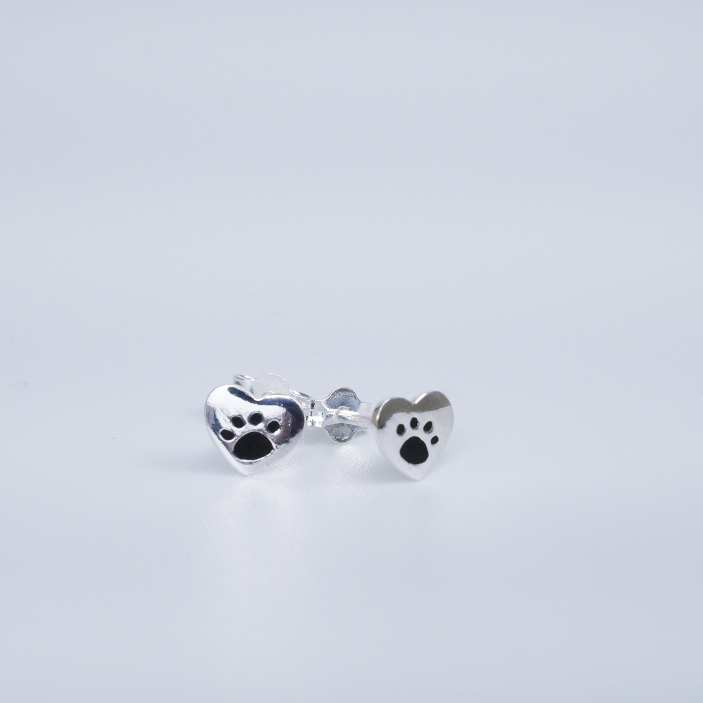 Silver paw print earrings on a light gray background