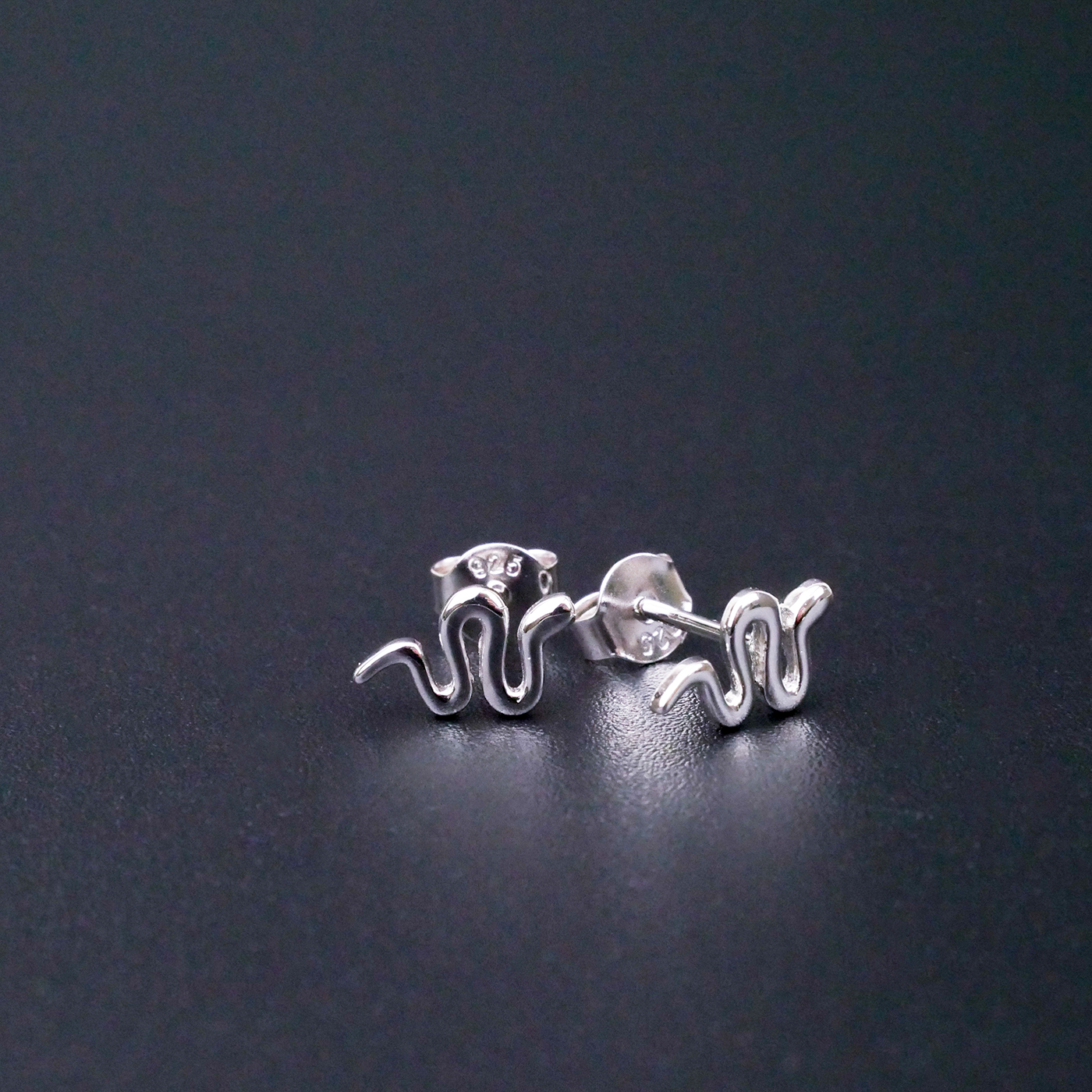 Silver snake-shaped earrings on a dark grey background
