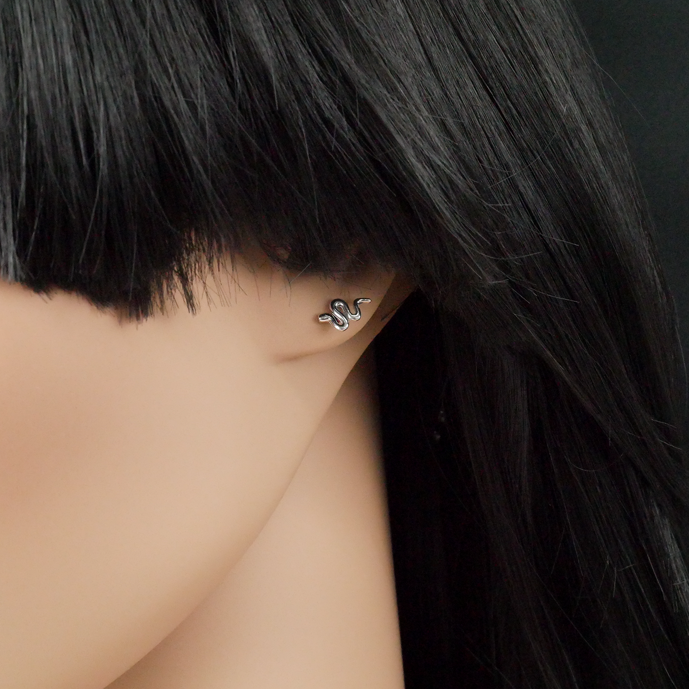 Close-up of an ear wearing a silver snake earring with black hair.