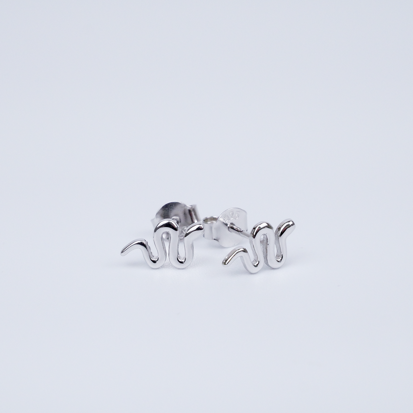 Silver snake-shaped earrings on a light grey background