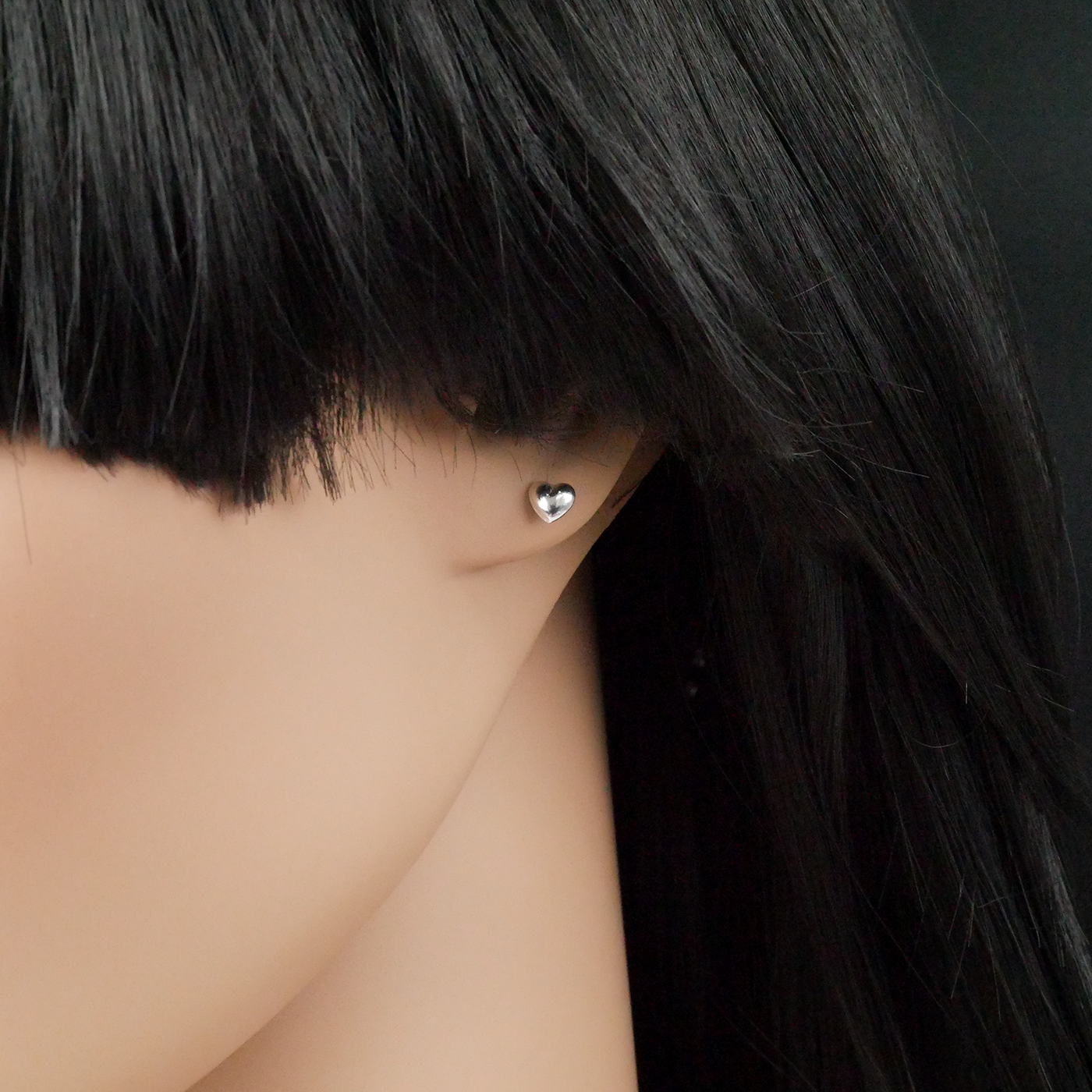 Close-up of a person wearing a silver heart-shaped earring with dark hair.