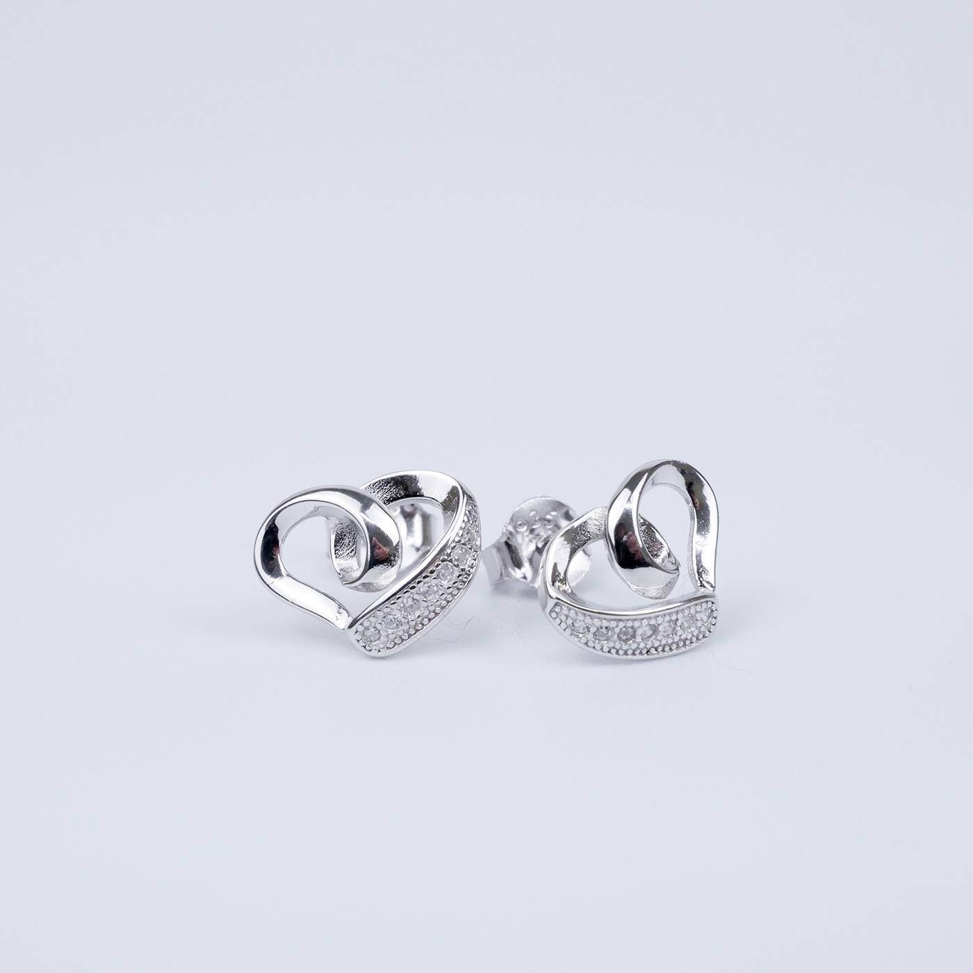 Pair of silver heart earrings with small zirconia on a light grey background