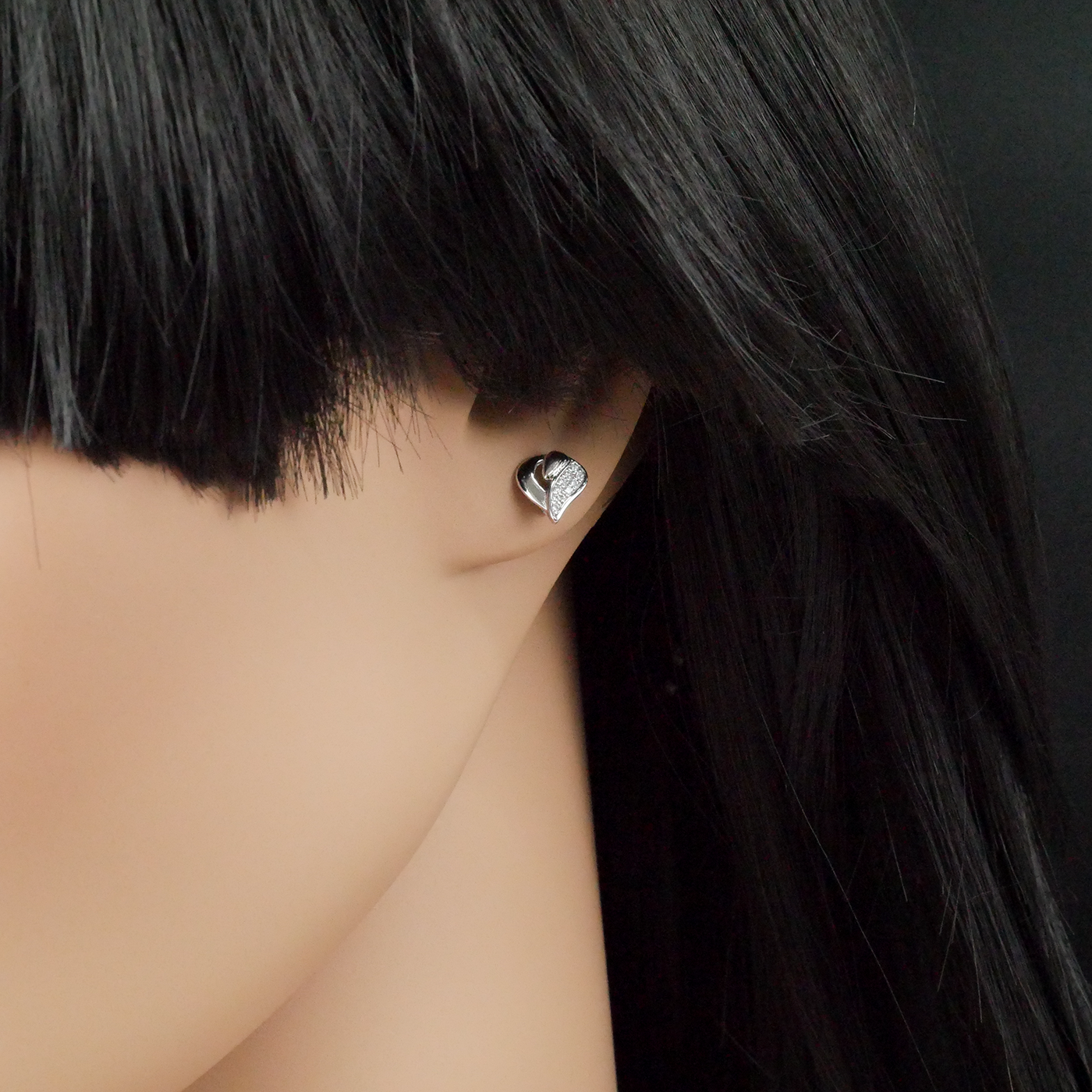 Heart-shaped earring worn by a person with black hair against a dark background