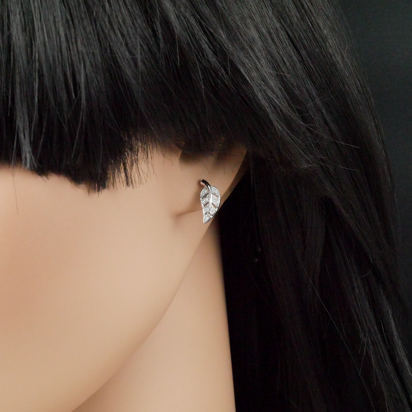 Close-up of a person wearing a silver leaf-shaped earring with dark hair.