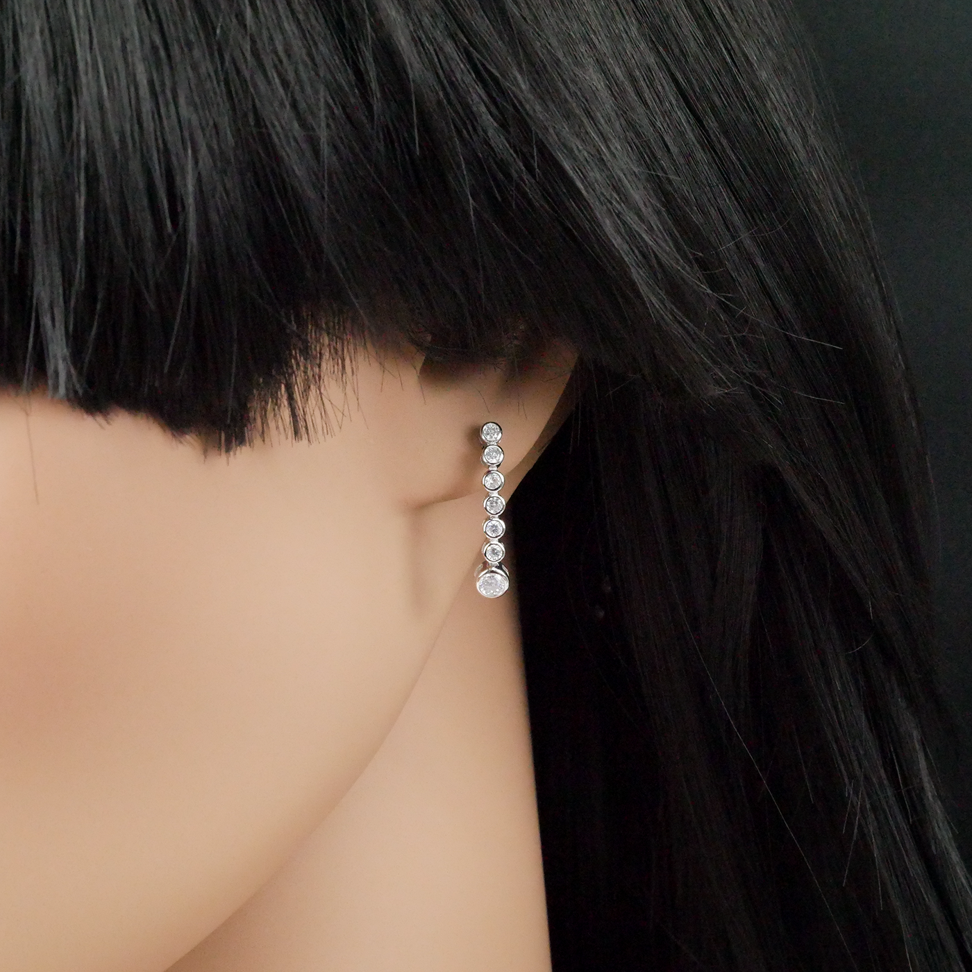 Close-up of a person wearing a dangling zirconia earring with a dark background