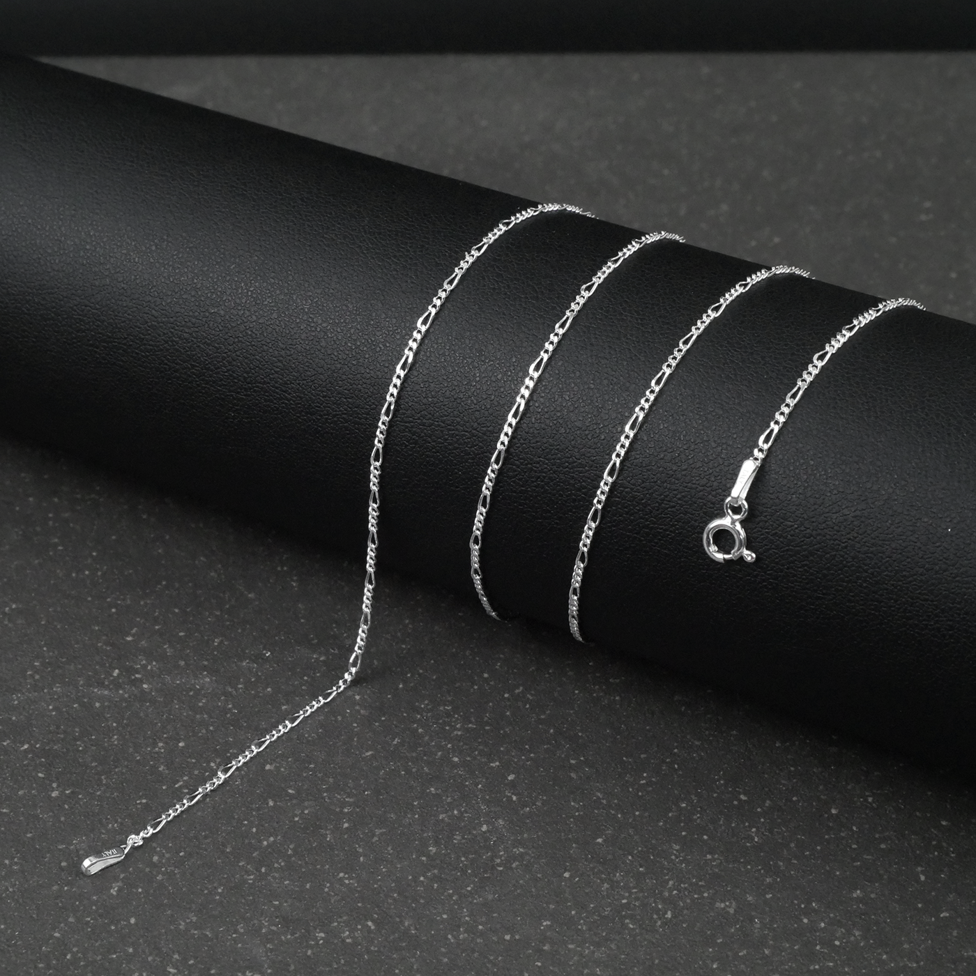 Silver fine figaro chain necklace on a black surface