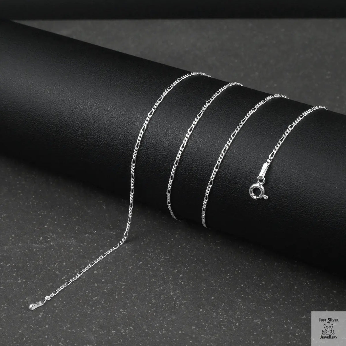 Silver fine figaro chain necklace on a black surface