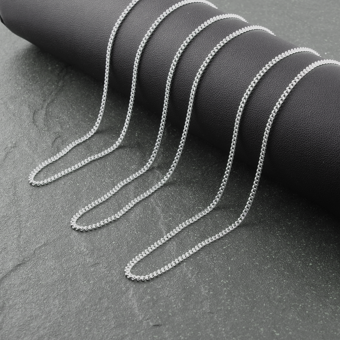 Silver chain necklace on a black cylindrical object against a gray background