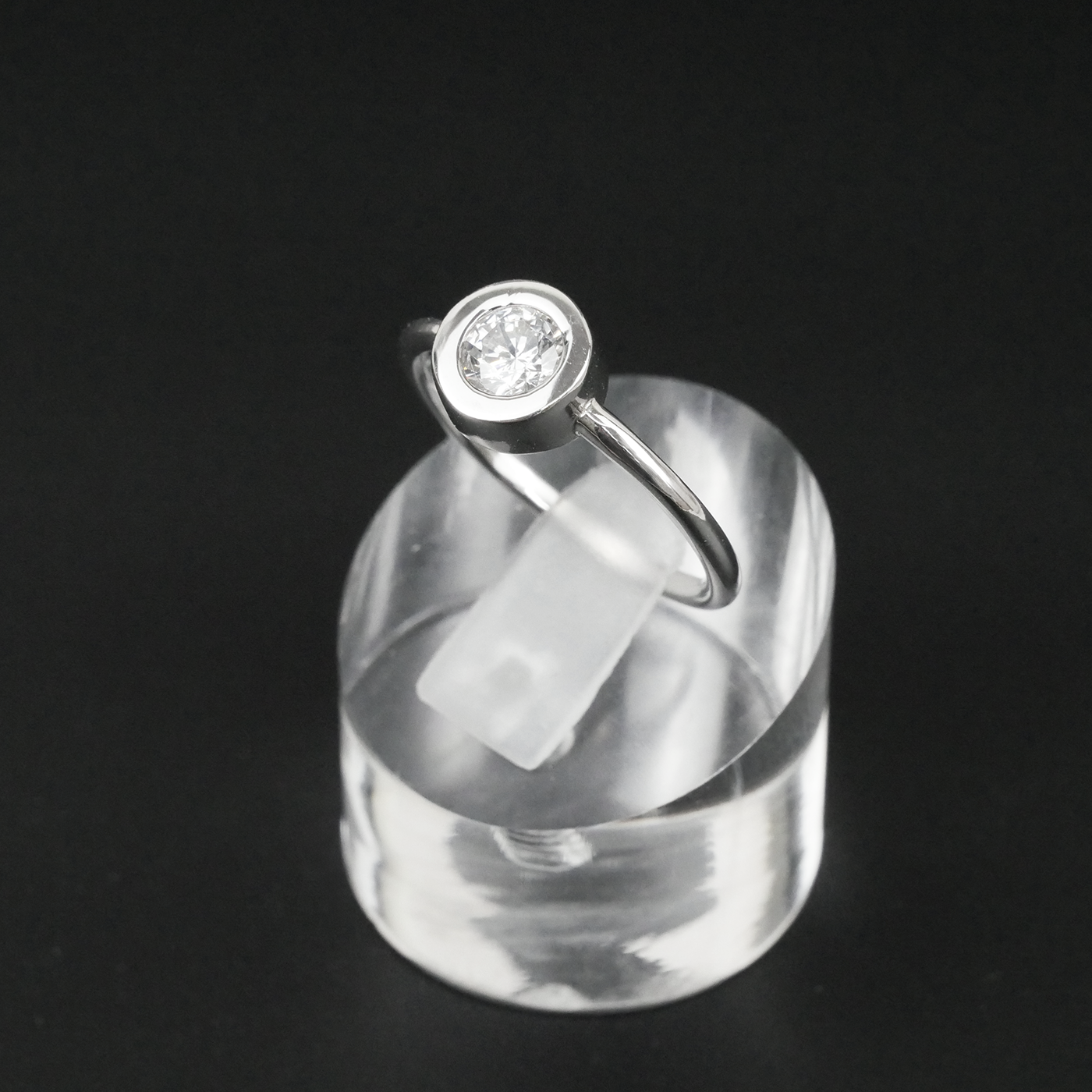 Silver ring with a CZ on a clear stand against a black background
