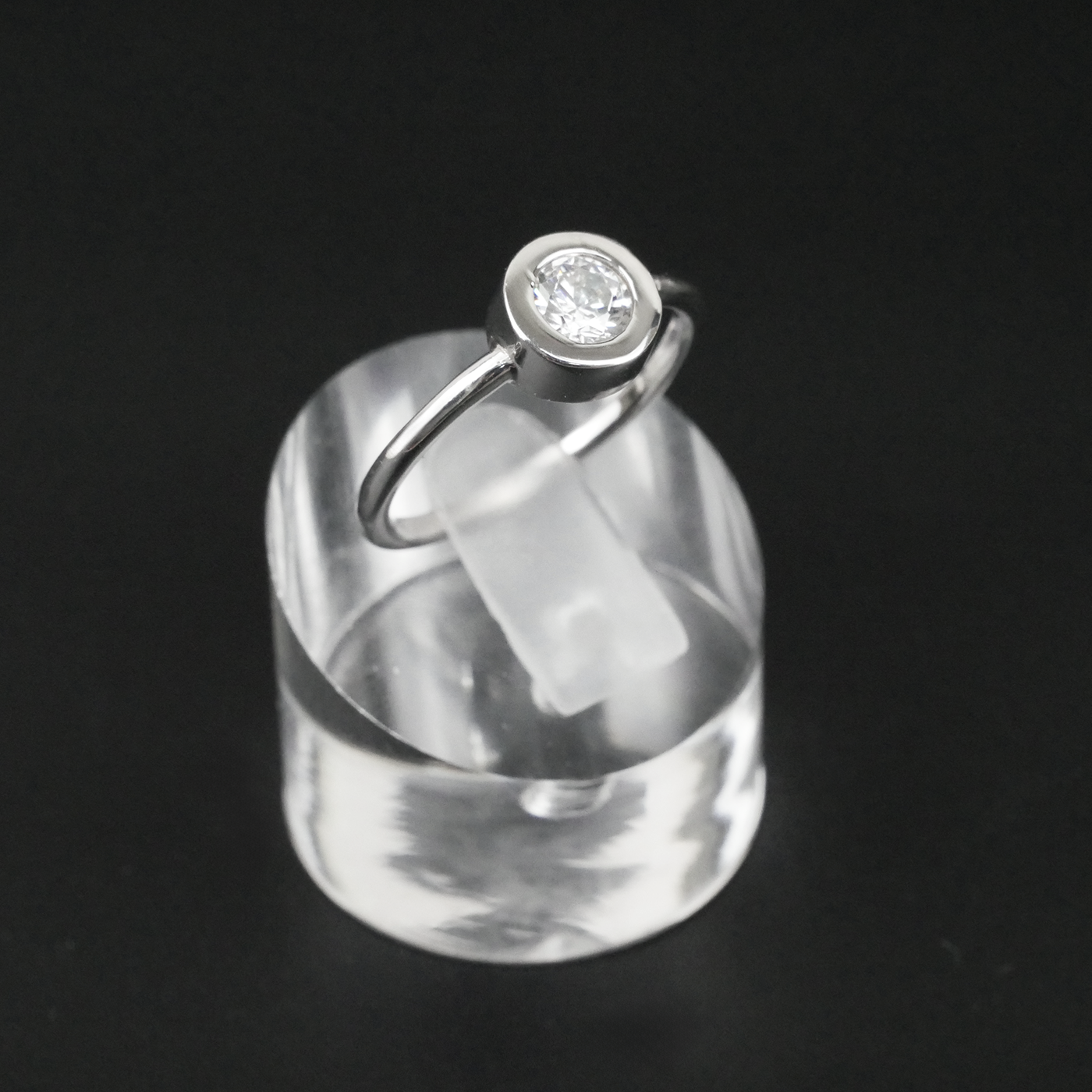Silver ring with a CZ on a clear stand against a black background