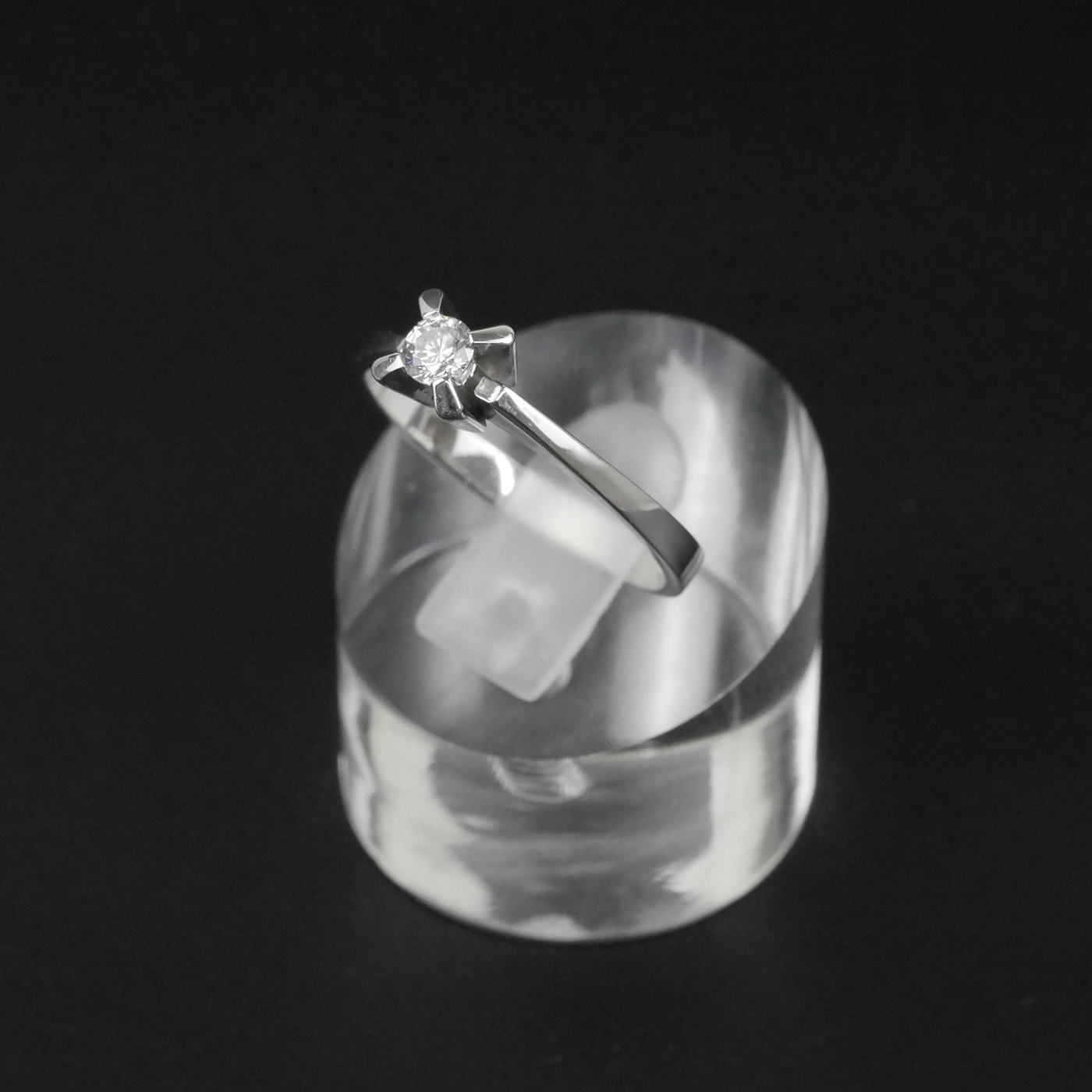 Silver ring with a CZ on a clear stand against a black background